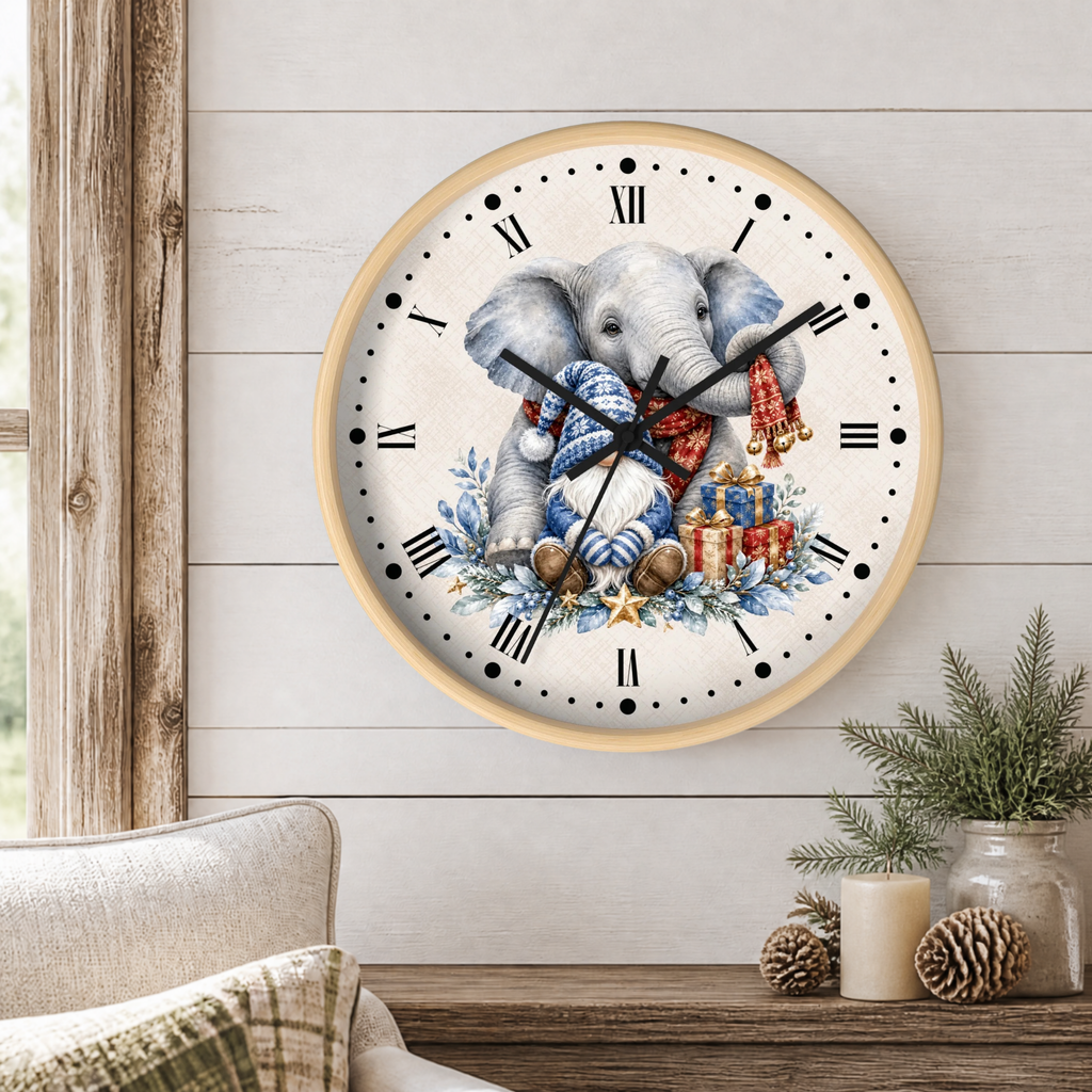A round wall clock with a light wood frame hangs on a white shiplap wall above a rustic wooden table. The clock face features a watercolor illustration of a baby elephant wearing a blue knit sweater and red scarf, surrounded by Christmas presents and evergreen branches.