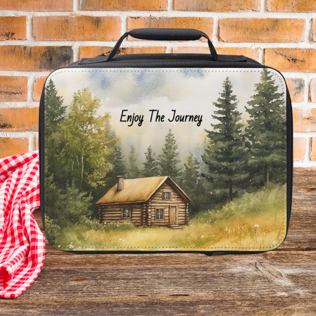 Lunch bag with a cabin design and 'Enjoy The Journey' text on a picnic table against a brick wall background