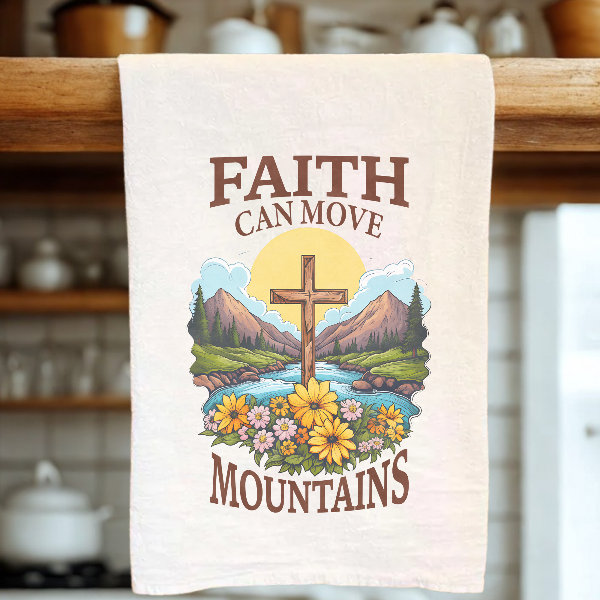 Tea towel with a cross and nature design, featuring the text 'Faith can move mountains', hanging on a wooden rack.
