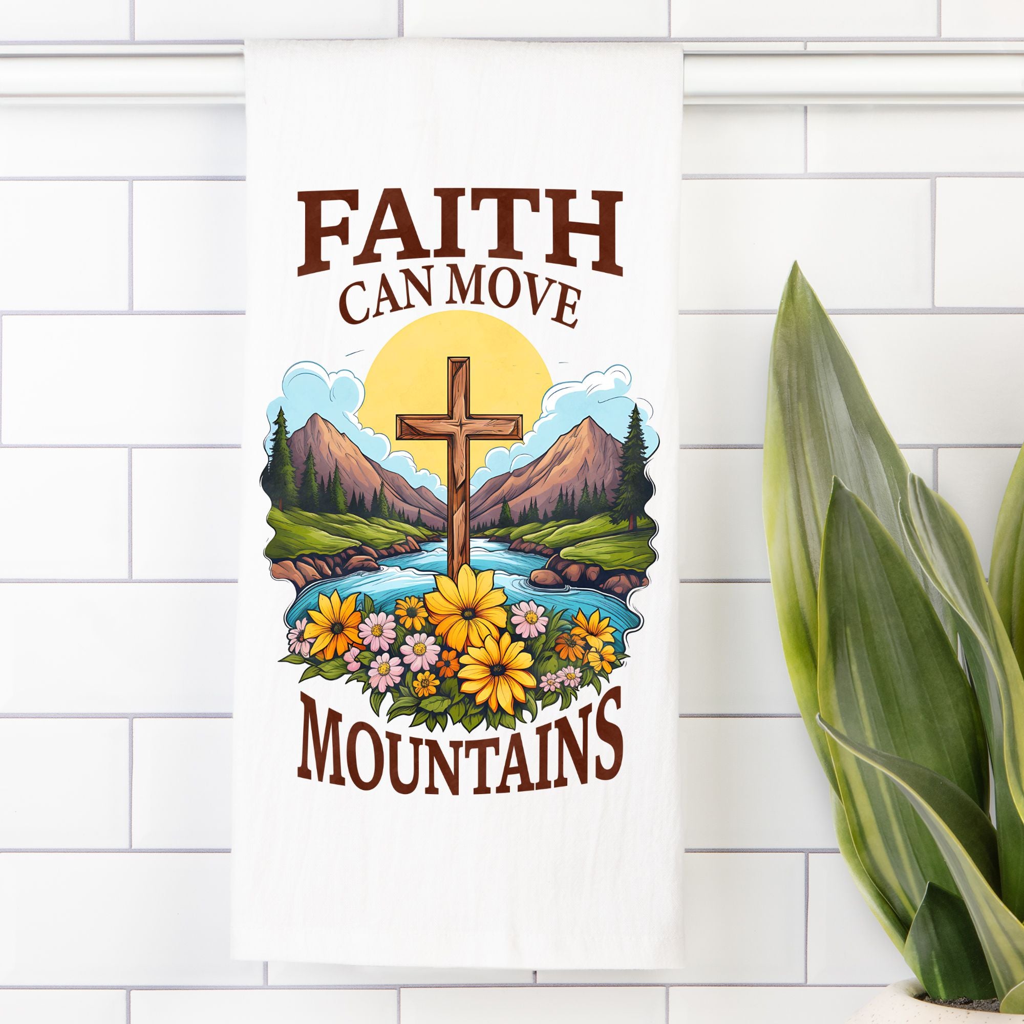 Decorative tea towel with cross, mountains, and flowers on a white tiled wall.
