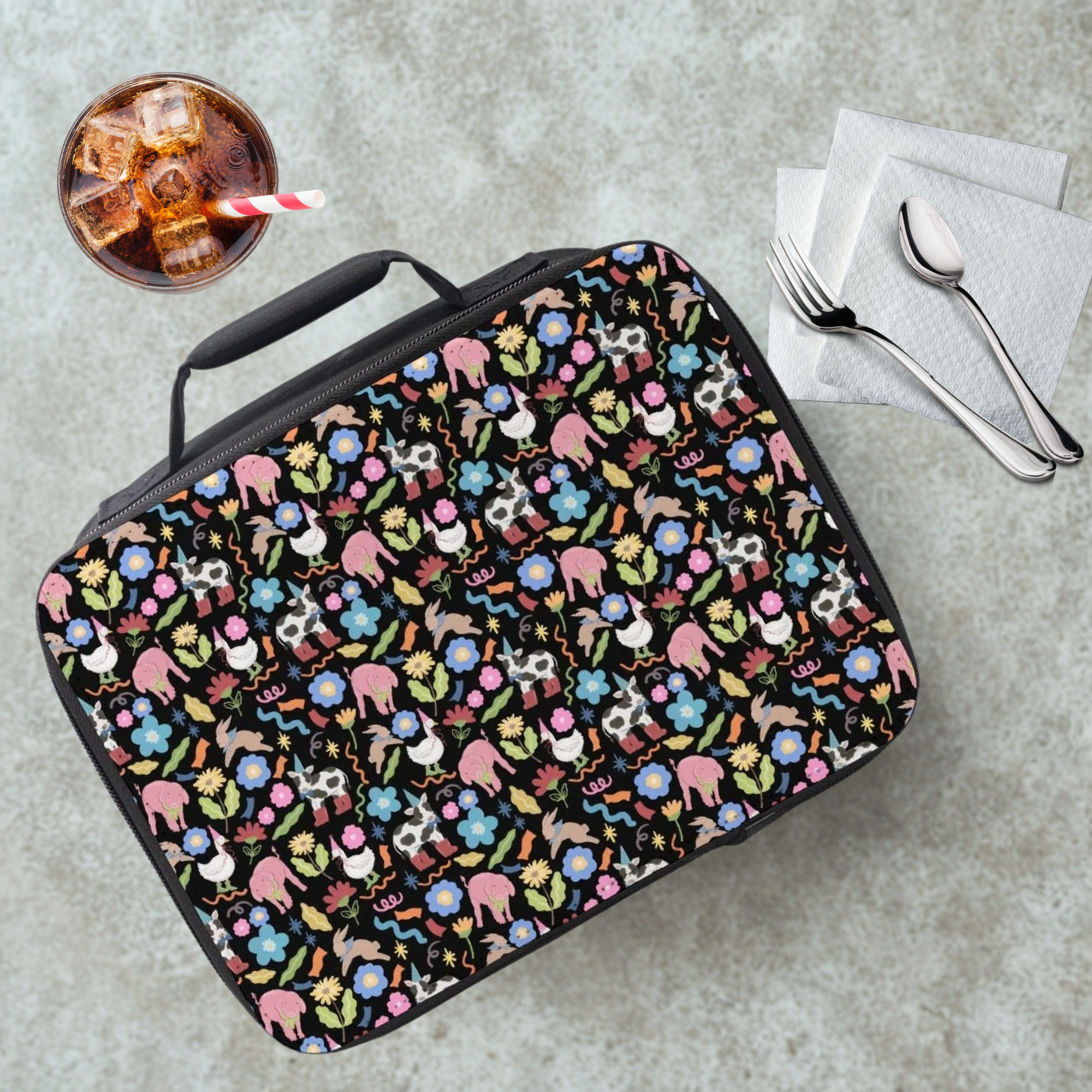  insulated lunch bag with colorful animal & flower pattern on a cafeteria table with a drink and utensils
