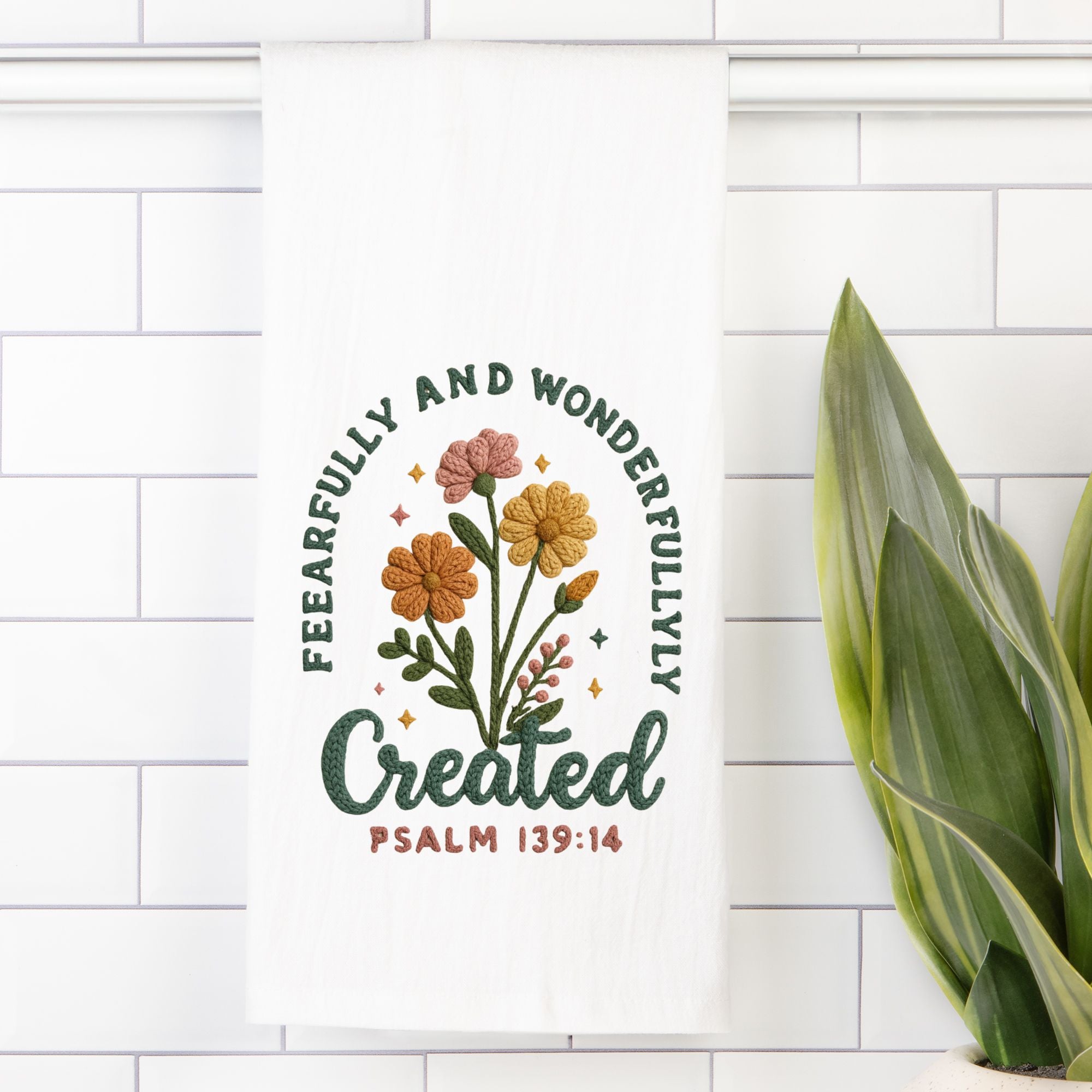 Decorative tea towel with floral design and text on a white tiled wall.
