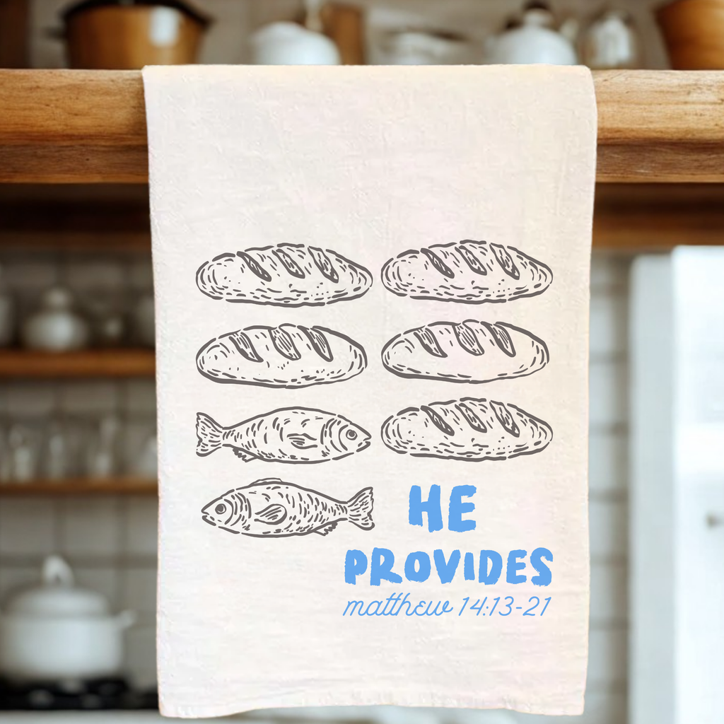 Kitchen towel with bread and fish illustrations and 'He Provides' text in a kitchen setting