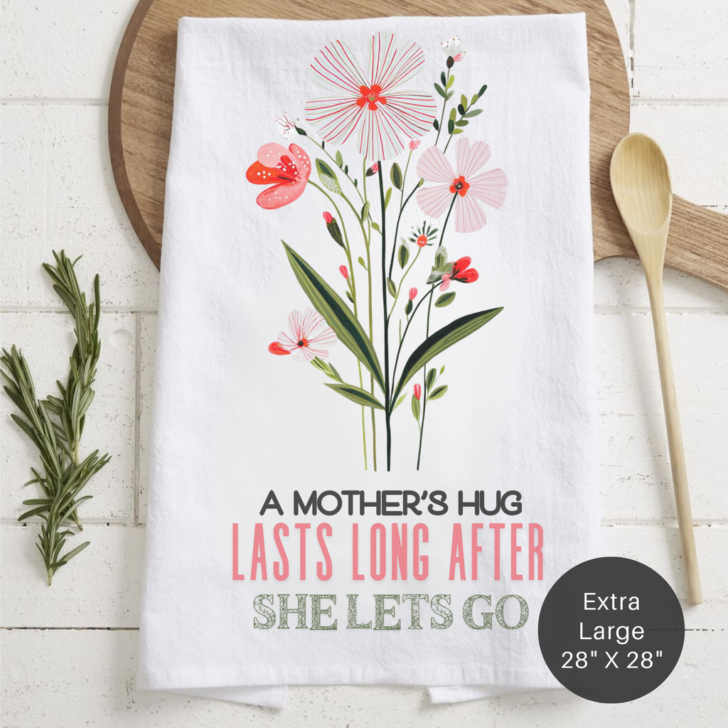 Floral-themed tea towel with text 'A Mother's Hug Last Long After She Lets Go' on a wooden surface