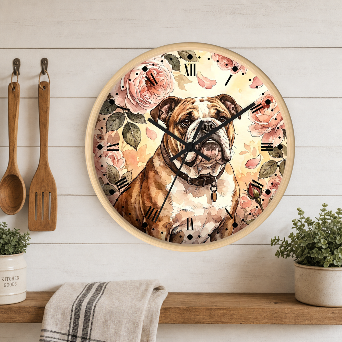 A round wall clock featuring a watercolor-style illustration of an English Bulldog surrounded by pink roses and green leaves, mounted on a white wood-paneled wall above a shelf with kitchen utensils and plants.