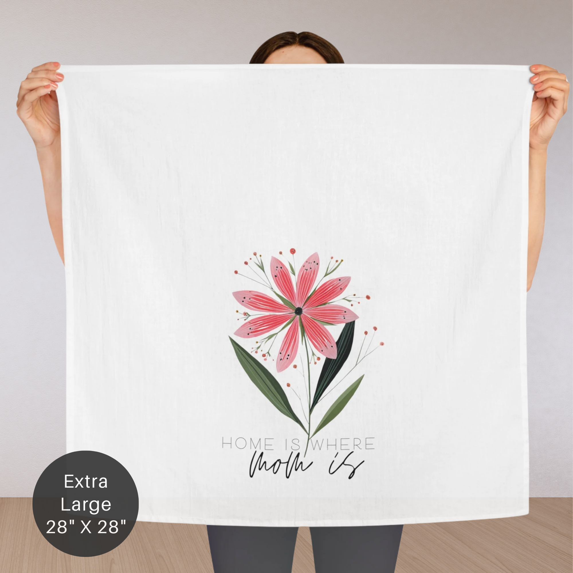 Person holding an extra large white tea towel with a pink flower design and text 'Home Is Where Mom Is'.