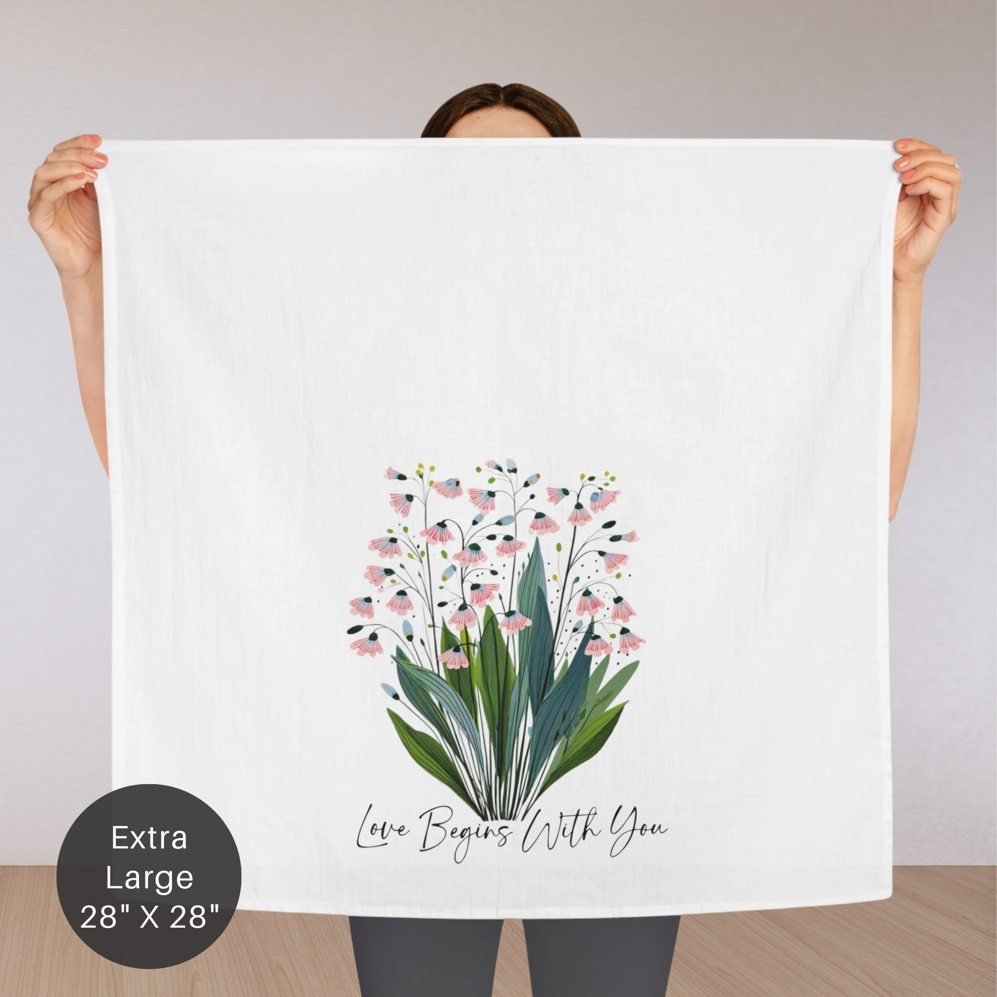Person holding an extra large white tea towel with floral design and text.