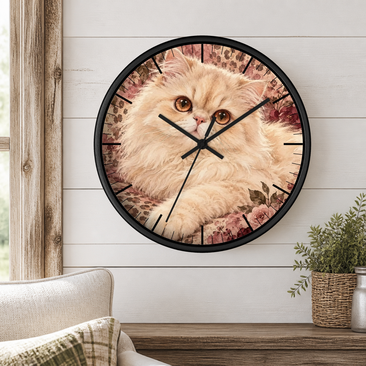 A round wall clock with a black frame and hands, featuring a fluffy cream-colored cat printed on the face, mounted on a white shiplap wall above a wooden console table with a small potted plant.