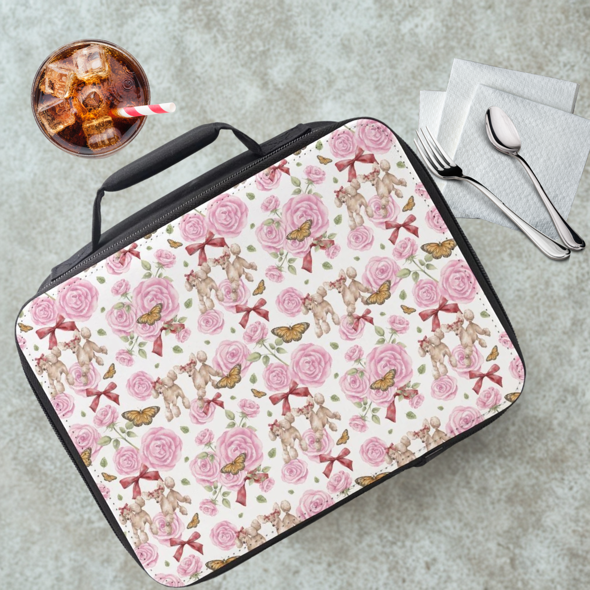 Lunch bag with poodle dogs, roses, butterflies, and bows pattern on a cafeteria table with a drink and utensils.