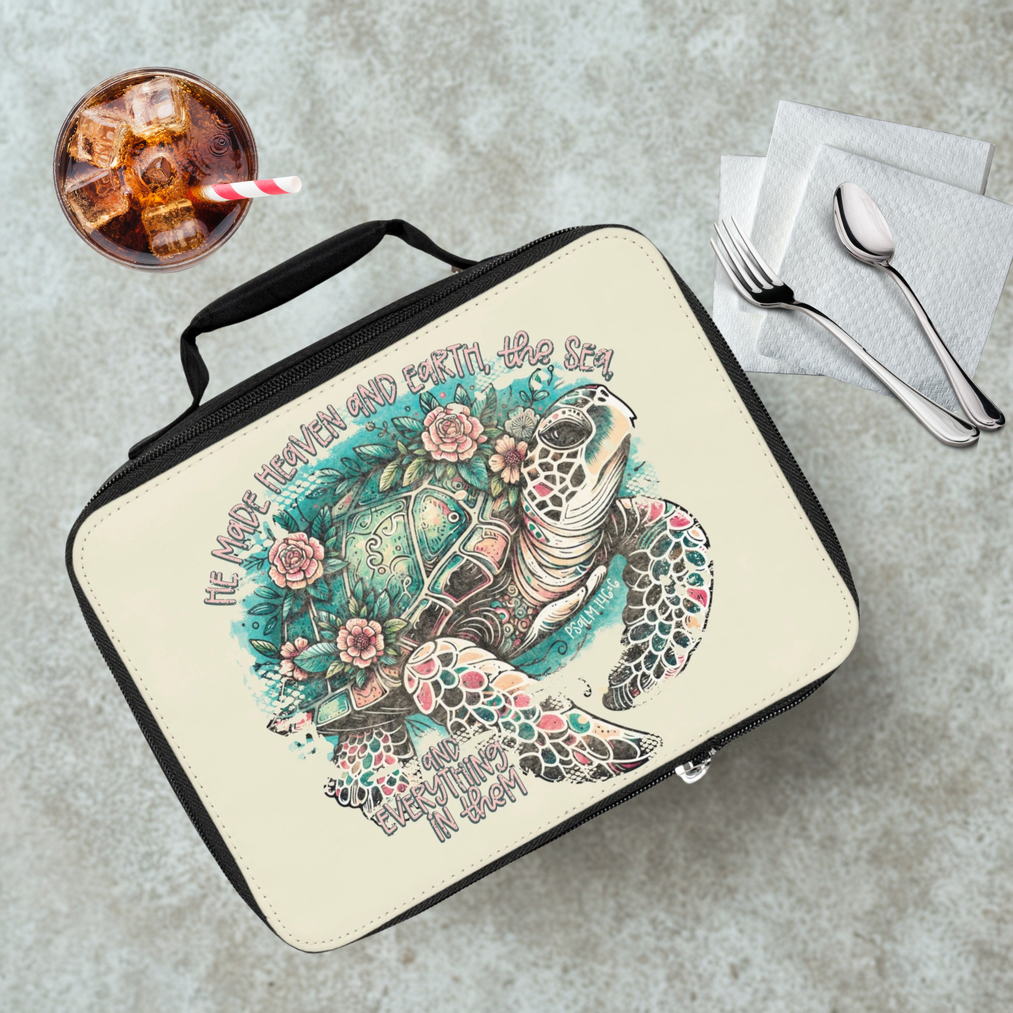  insulated lunch bag with a turtle design on a cafeteria table with a drink and eating utensils.