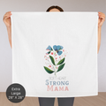 Person holding an extra large cotton tea towel with floral design and text 'Soft Heart Strong Mama' on a plain background