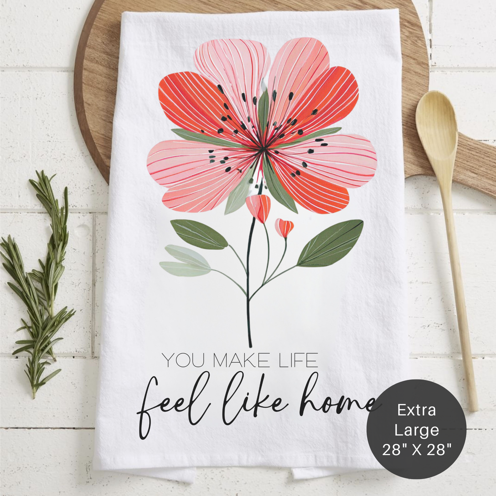 Folded floral tea towel with text 'You Make Life Feel Like Home' on a wooden surface