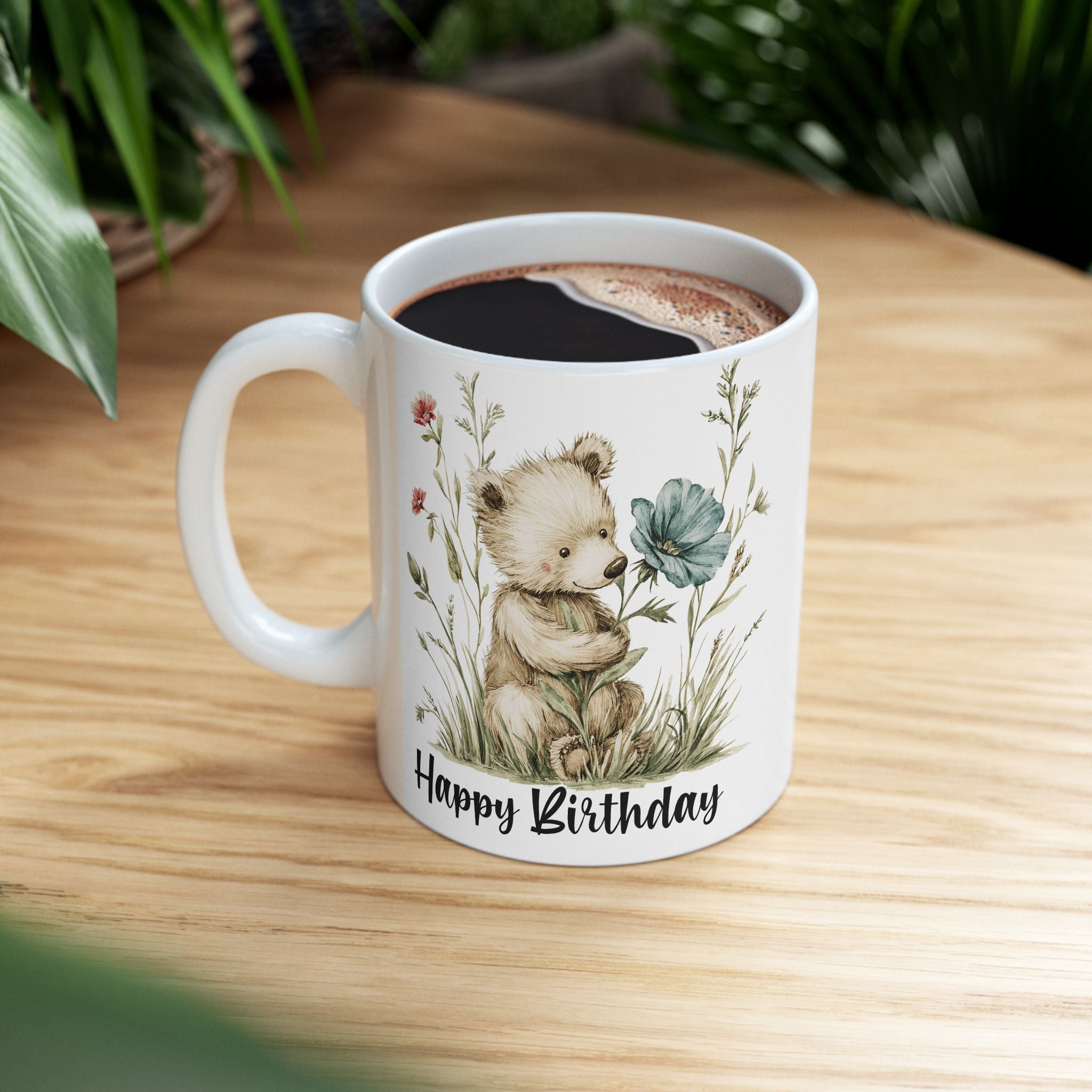 White mug with a bear and floral design, filled with coffee, on a wooden surface.