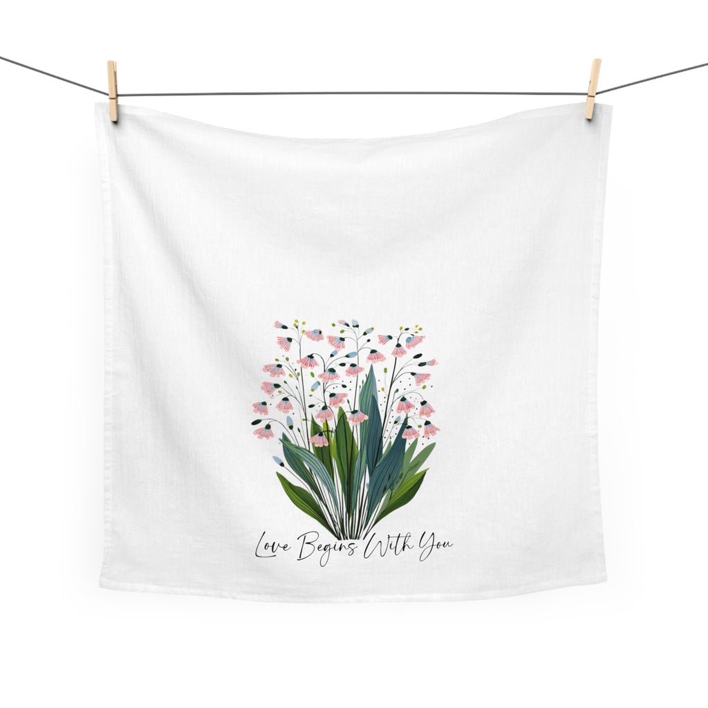 White towel with floral design and text 'Love Begins With You' hanging on a line.