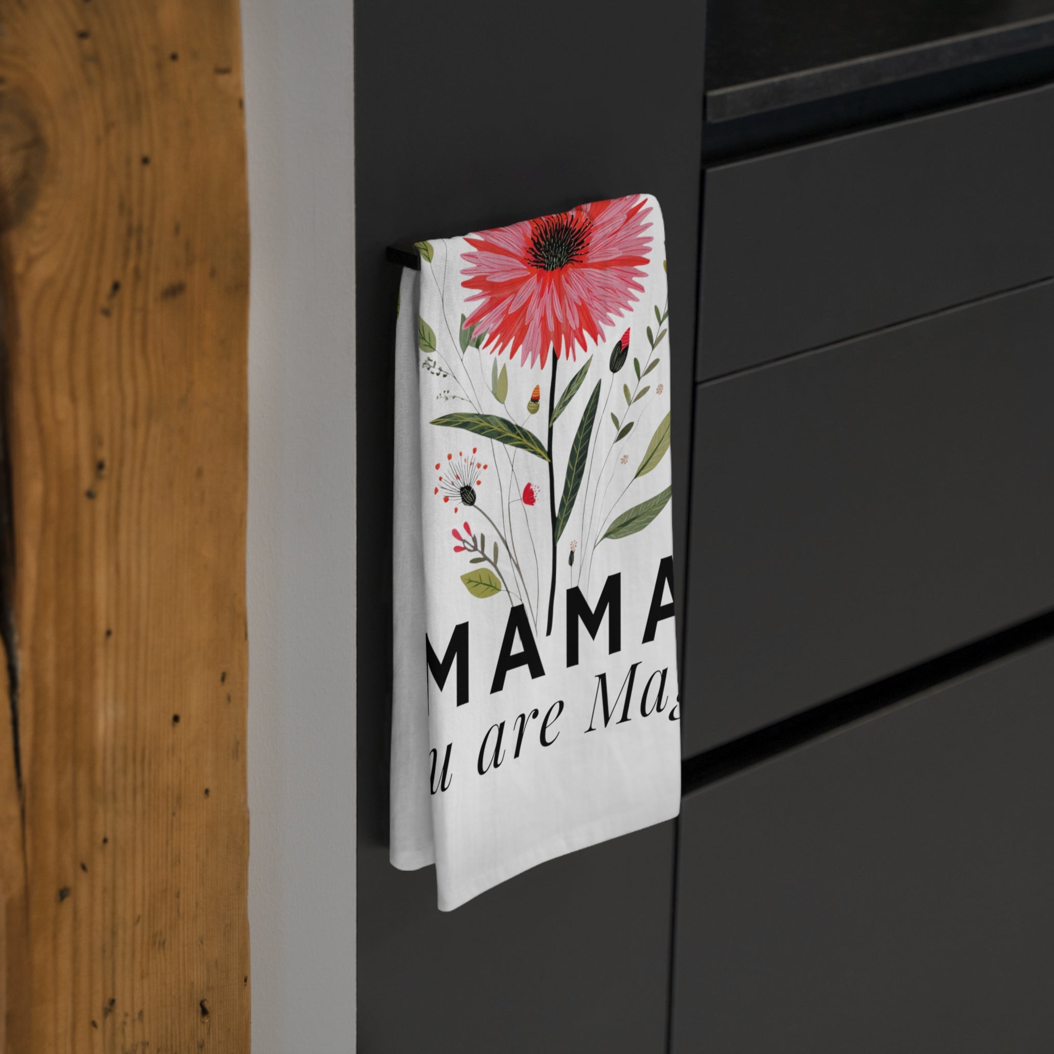 Folded floral tea towel with 'Mama you are magic' text hanging on a black cabinet.