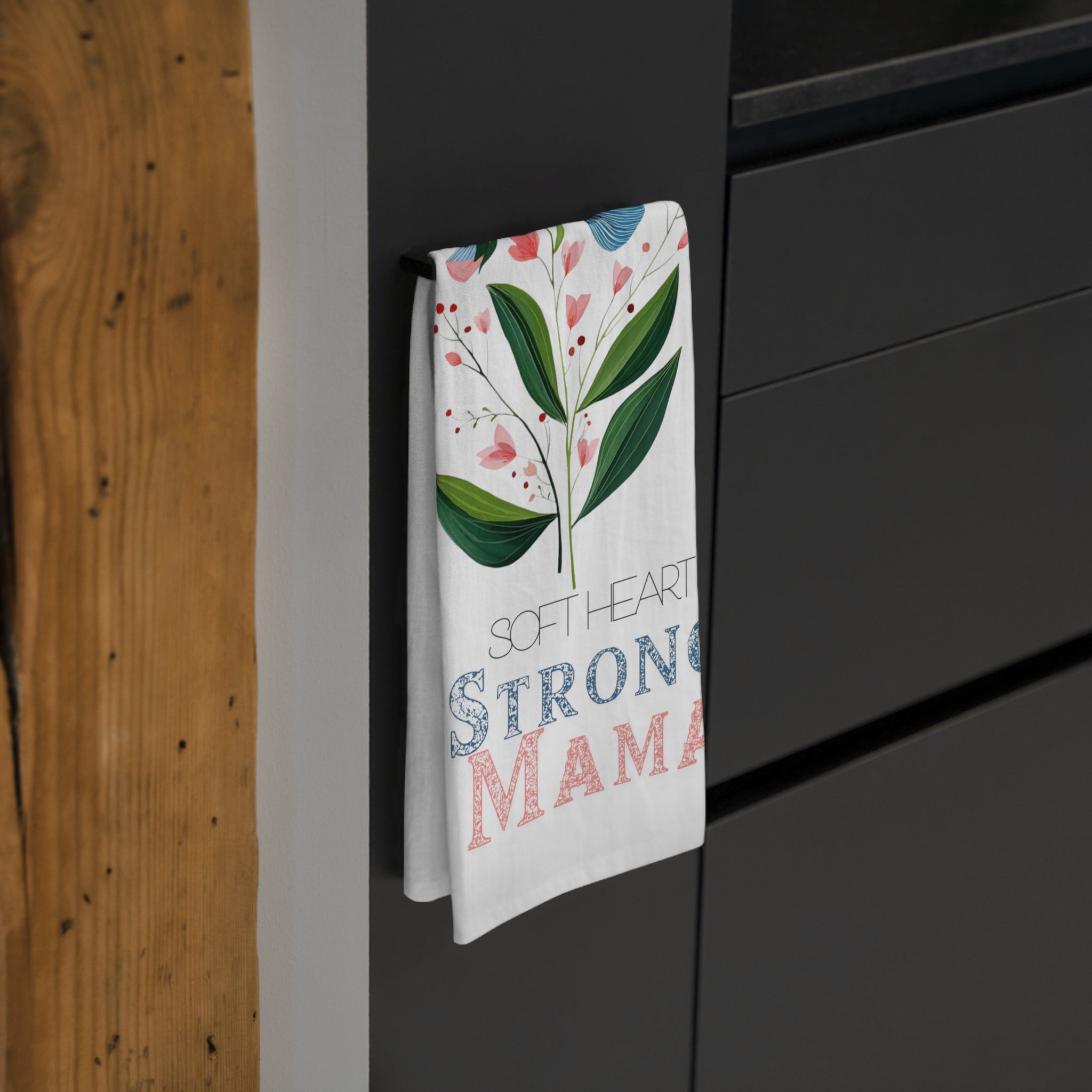 Tea towel with floral design and text hanging on a black cabinet.