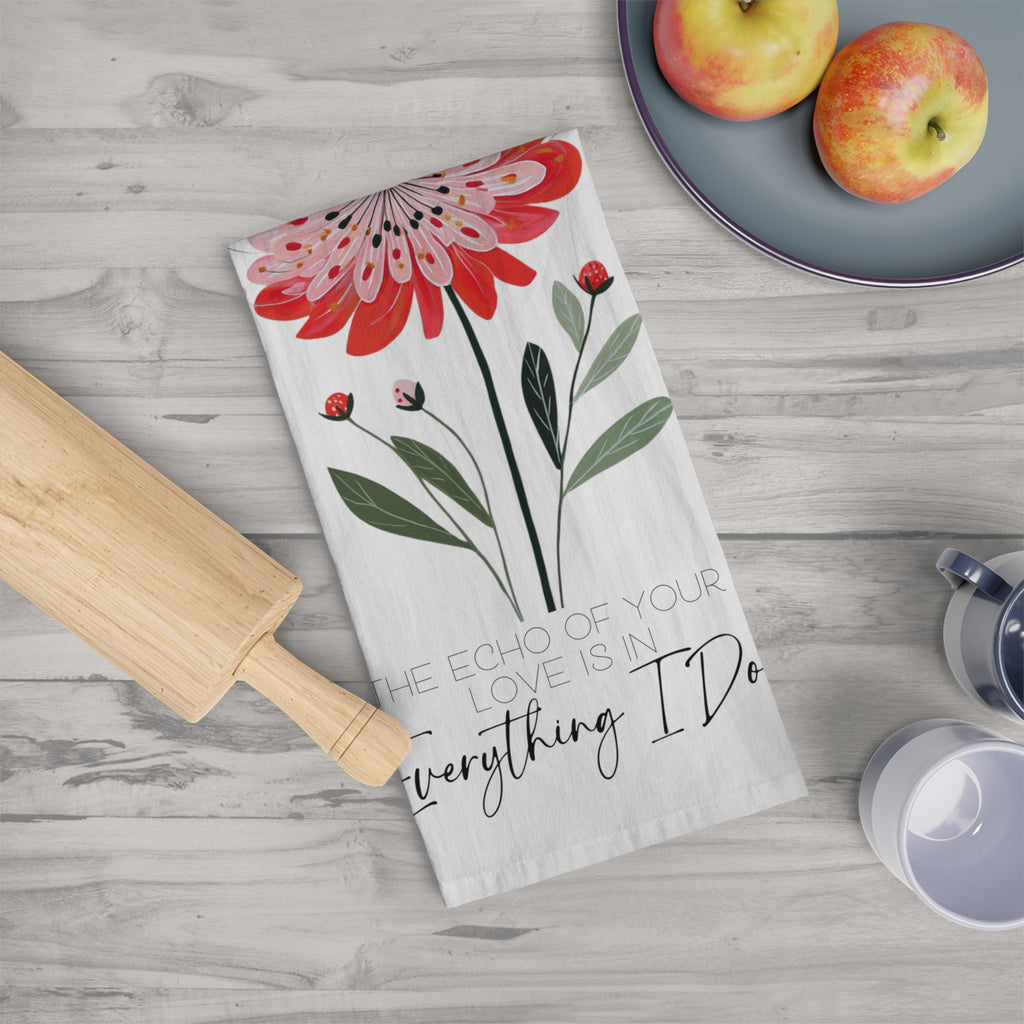 Floral-themed kitchen towel with text on a wooden surface with apples and a rolling pin.