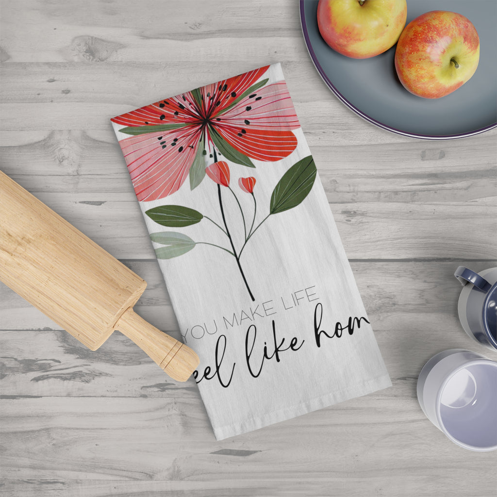 Folded floral tea towel with text on a wooden table with apples and a rolling pin.