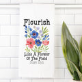 Decorative tea towel with floral design and text on a white tiled wall.