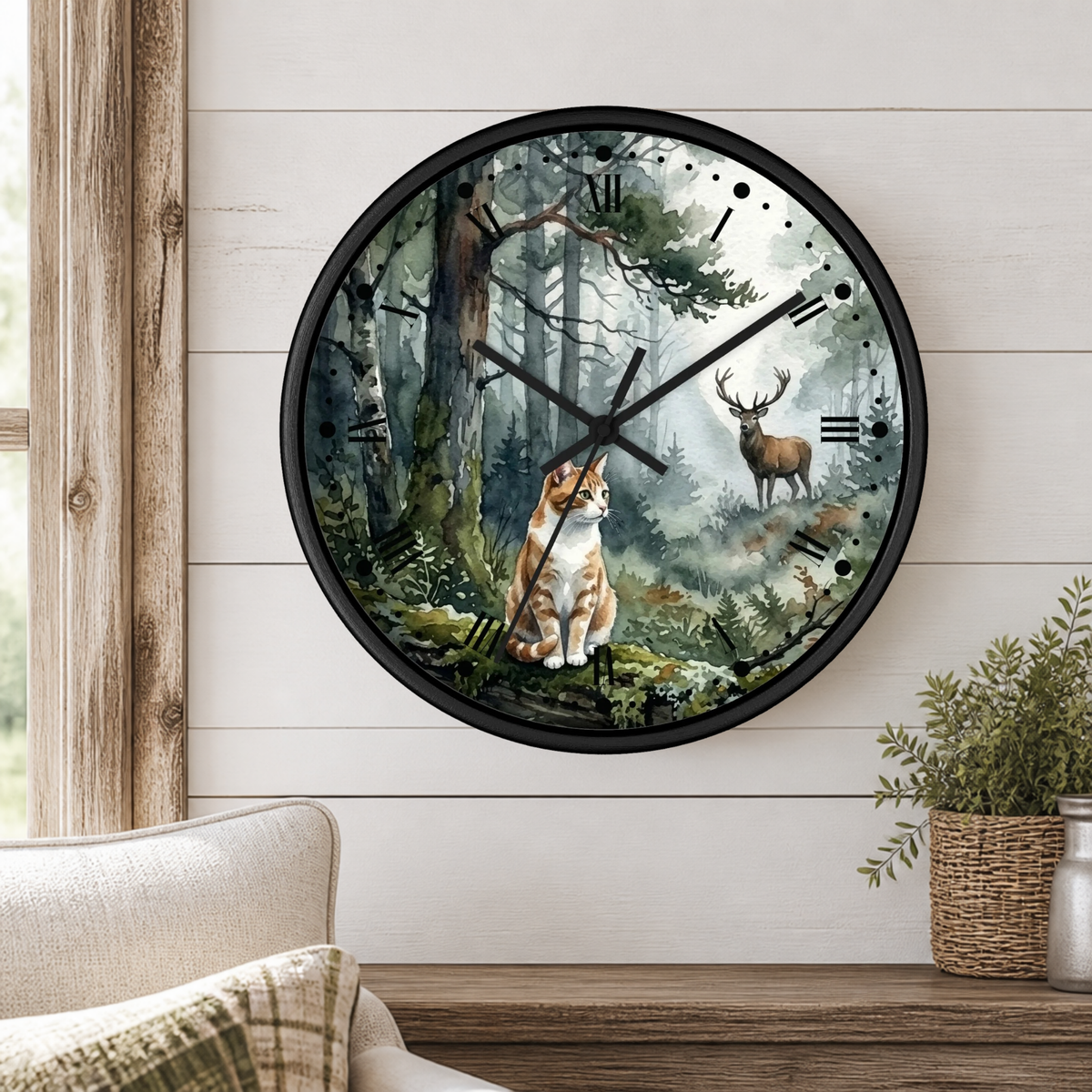 A round wall clock with a black frame and a forest illustration featuring a cat and deer, mounted on a white shiplap wall above a wooden table with a plant.