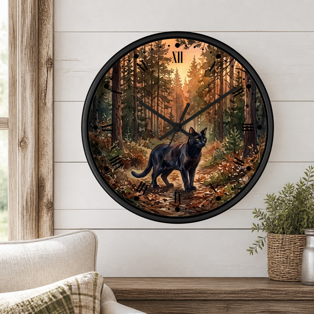 Round wall clock with a black cat walking through a forest at sunset, mounted on a white shiplap wall above a wooden mantel with a plant and cushion.