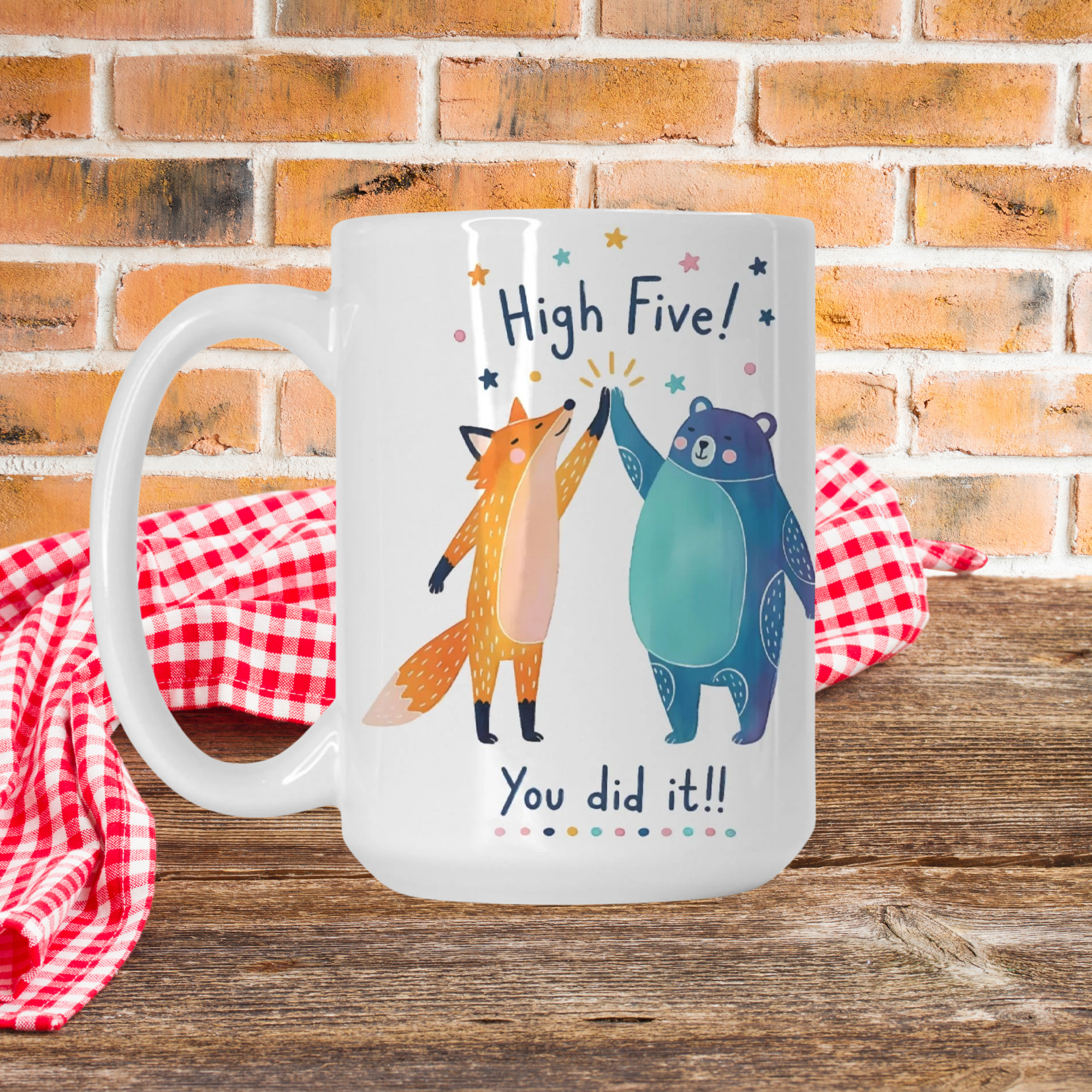 Mug with a design of a fox and bear high-fiving, text 'High Five! You did it!!', on a wooden surface with a brick wall background.