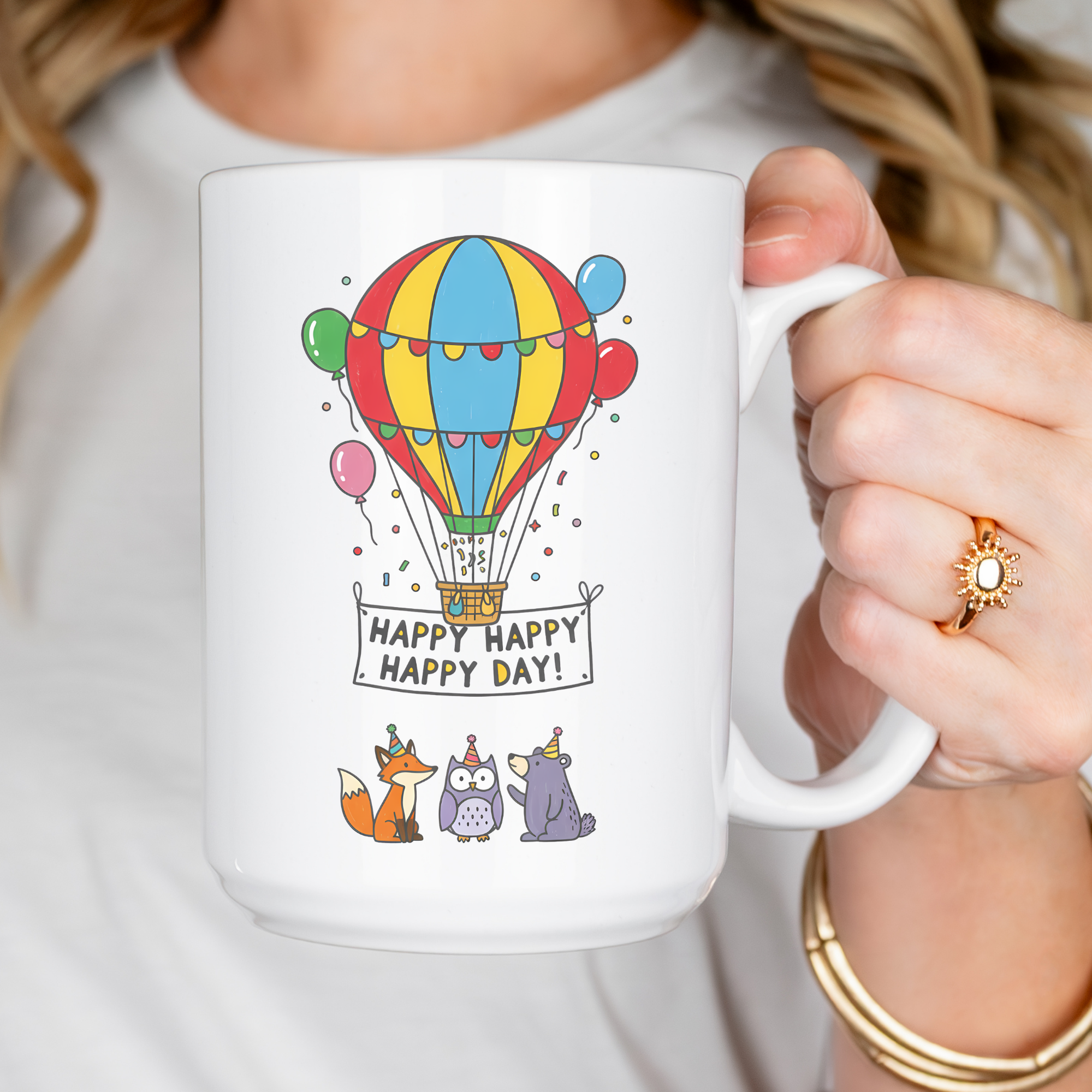 Person holding a mug with a colorful hot air balloon design and 'Happy Happy Happy Day!' text.