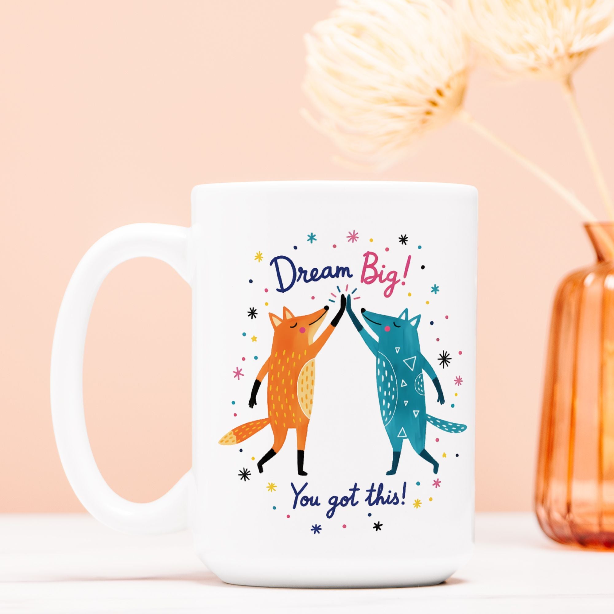White mug with foxes high fiving and 'Dream Big! You got this!' text on a pink background