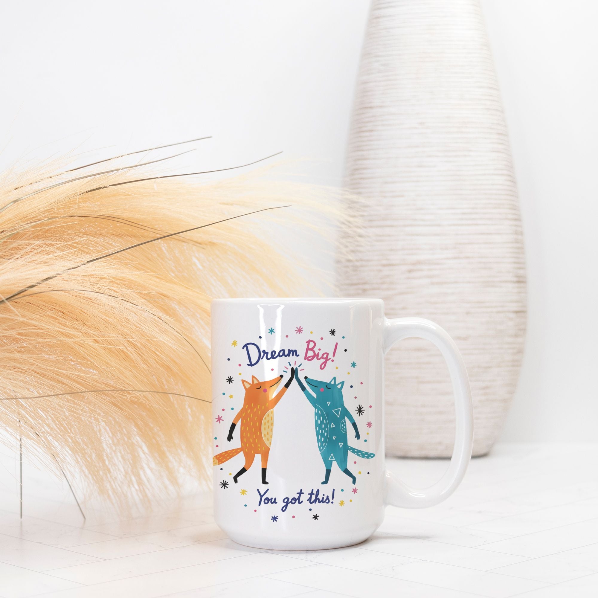 Mug with foxes and motivational text on a white surface with decorative elements