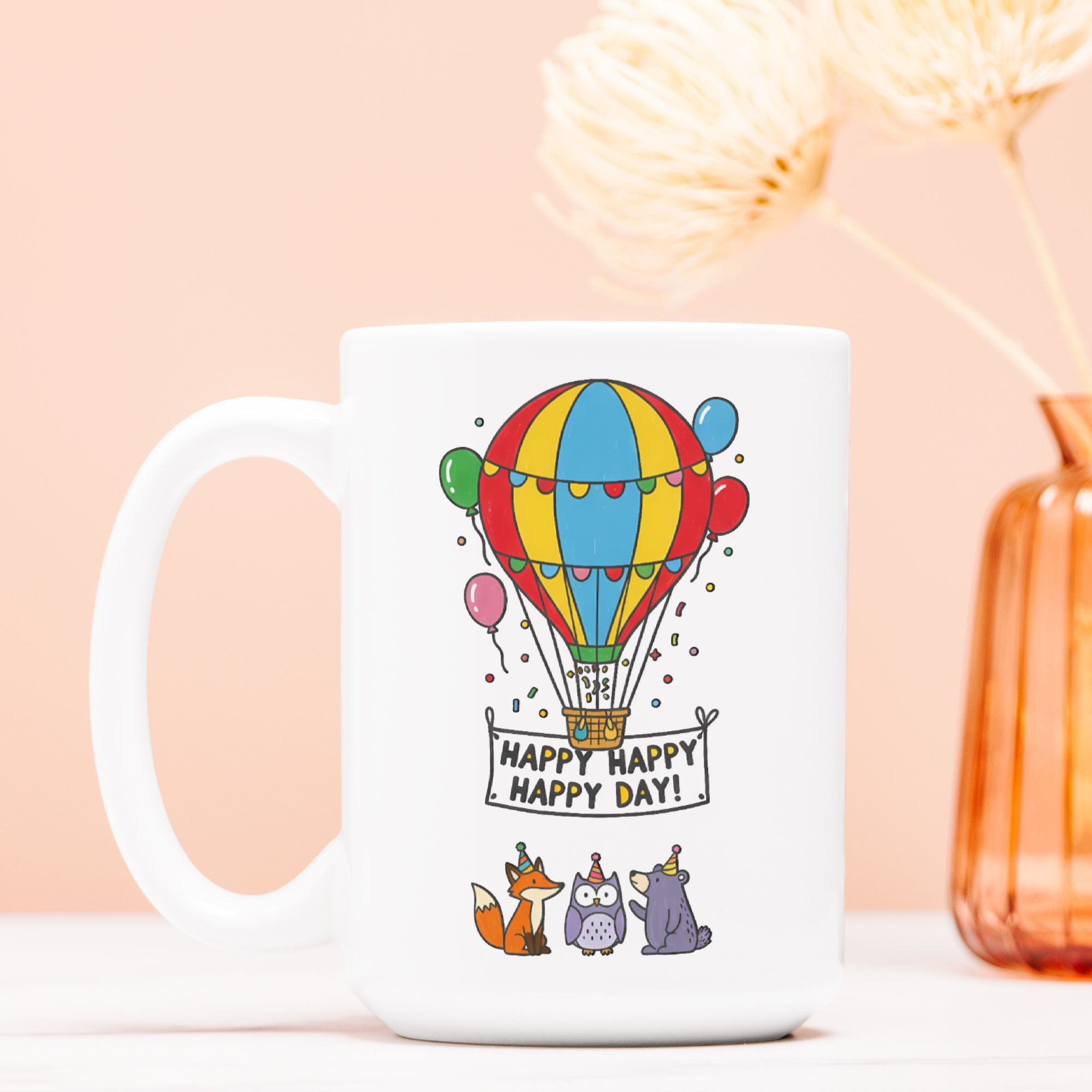 White mug with colorful hot air balloon design and 'Happy Happy Happy Day!' text on a light pink background.
