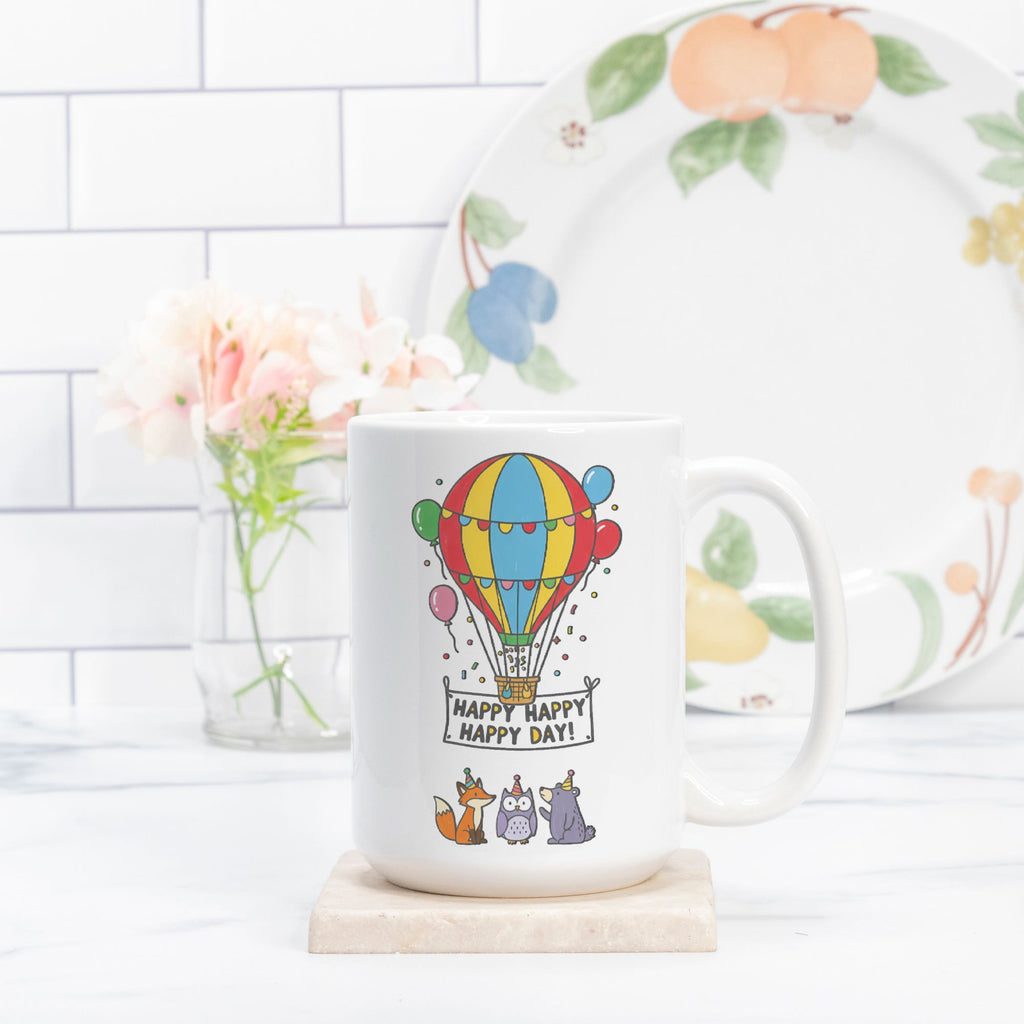 White mug with hot air balloon design and 'Happy Happy Day!' text on a white surface.