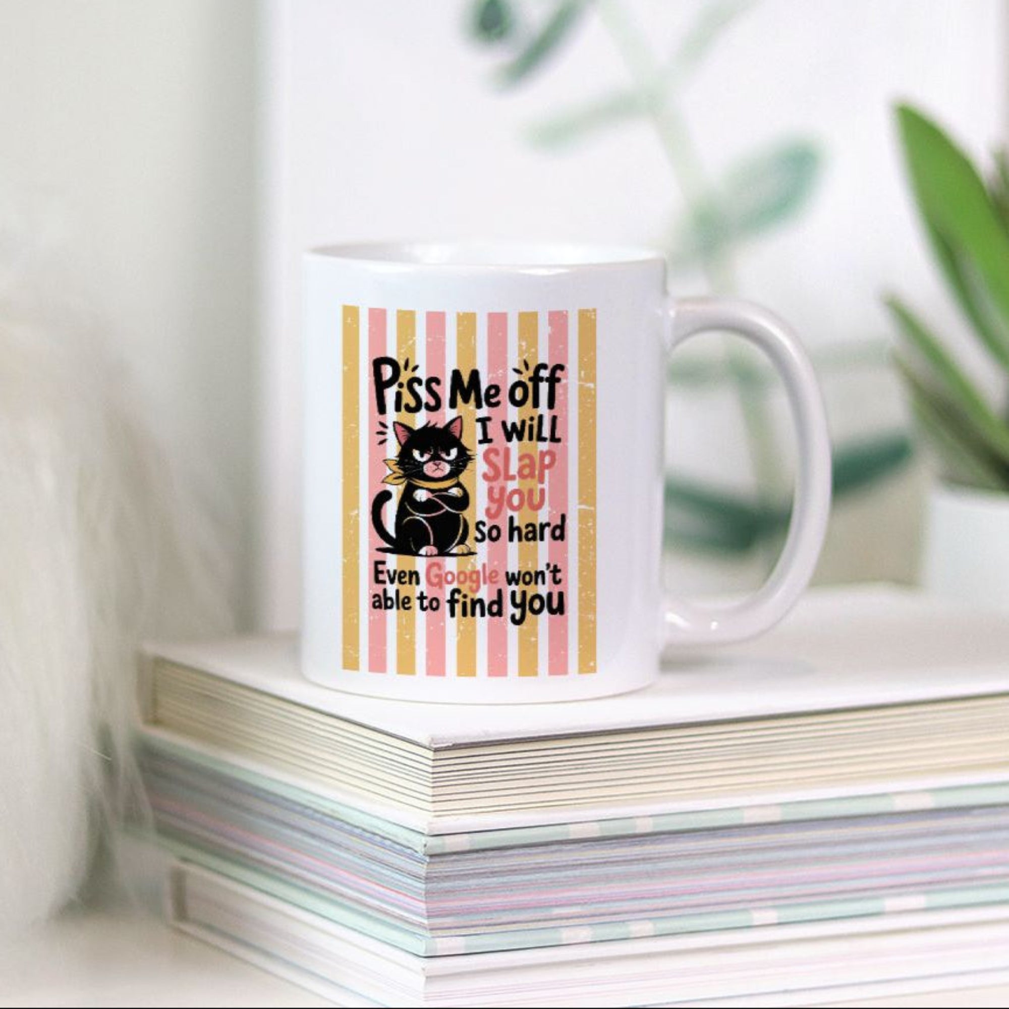 Mug with a humorous cat design on a stack of books with a plant in the background
