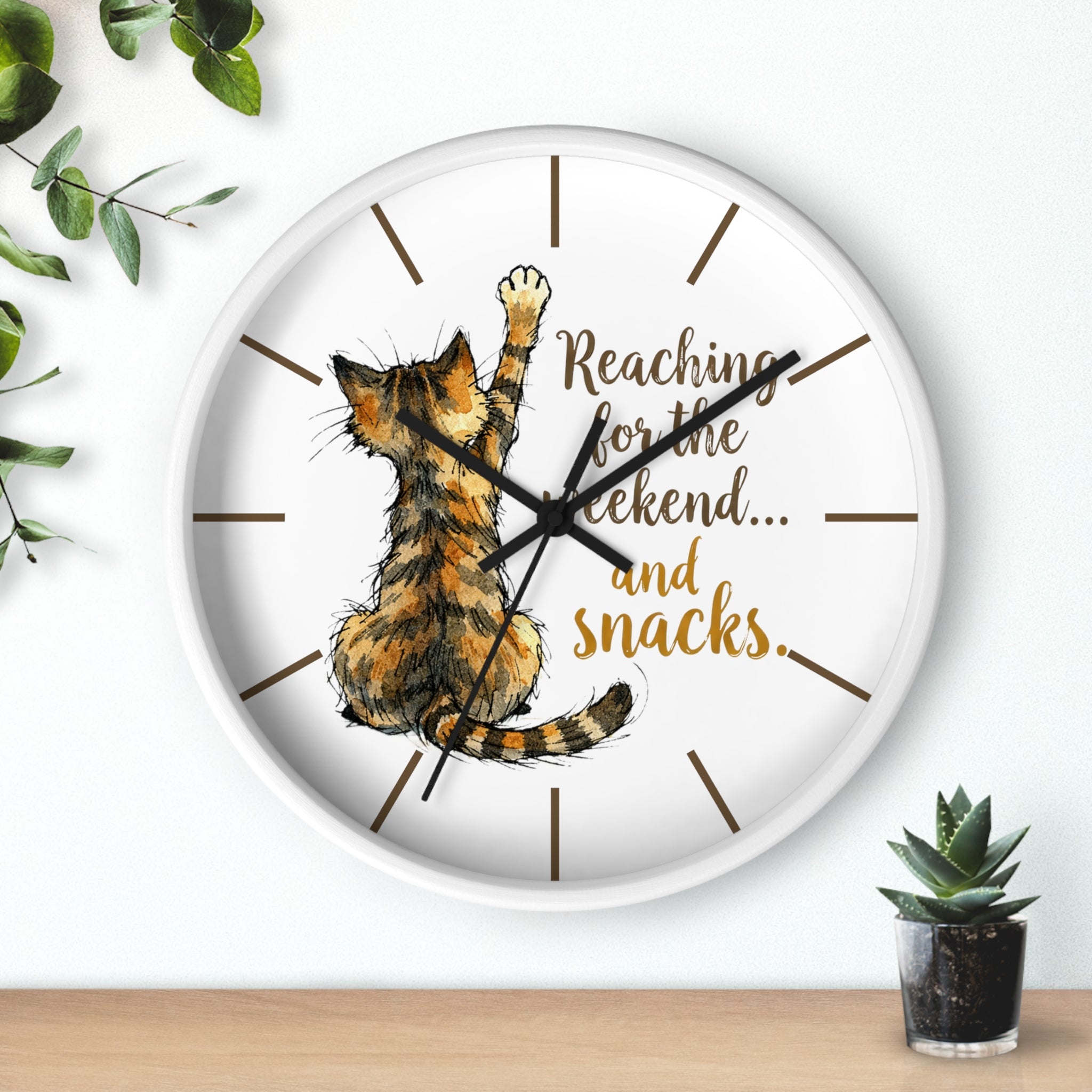 Round white wall clock with a cat illustration and text 'Reaching for the weekend... and snacks.' on a white background