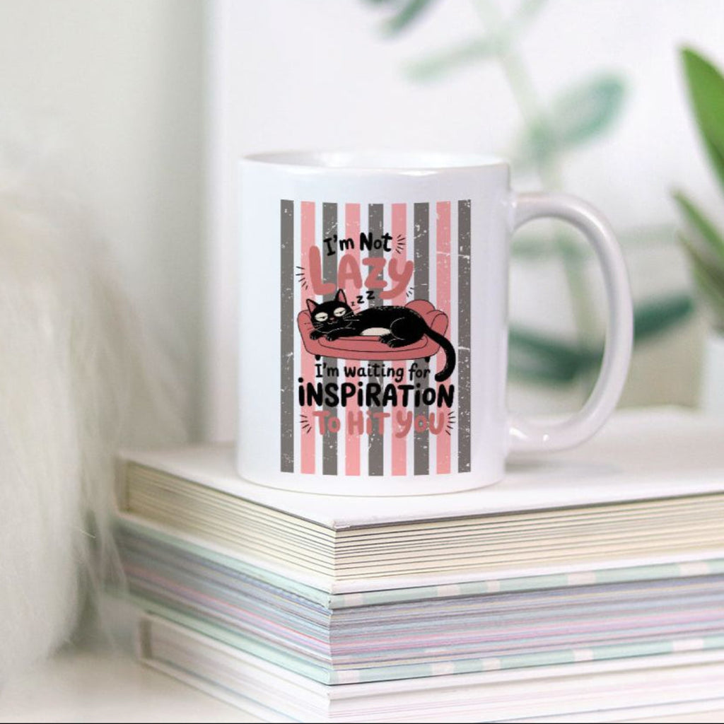 White mug with a black cat design and text on a stack of books with a plant in the background
