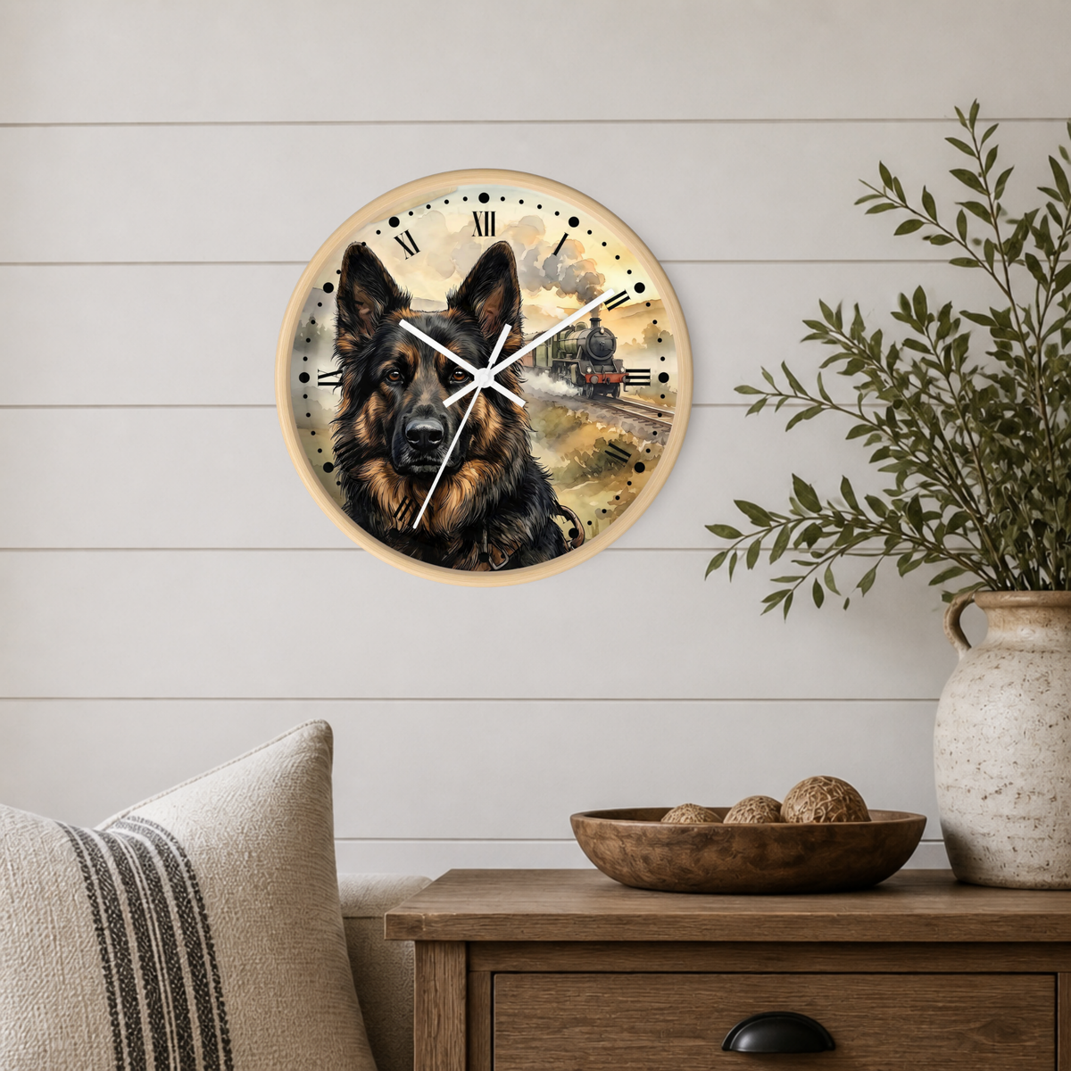 A round wall clock with a German Shepherd portrait and a small train illustration, mounted on a white shiplap wall above a wooden side table with a vase and bowl.