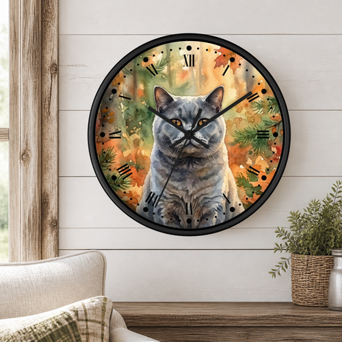 Round wall clock with a black frame featuring a gray tabby cat illustration over an autumn leaf background, mounted on a white shiplap wall above a wooden console table with a plant and part of a sofa visible.