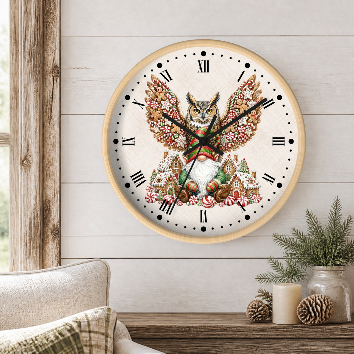A round wall clock with a light wood frame hangs on a white shiplap wall above a rustic table. The clock face features a detailed illustration of an owl with large wings decorated with pinecones and candy canes, surrounded by small gingerbread houses and snowflakes.