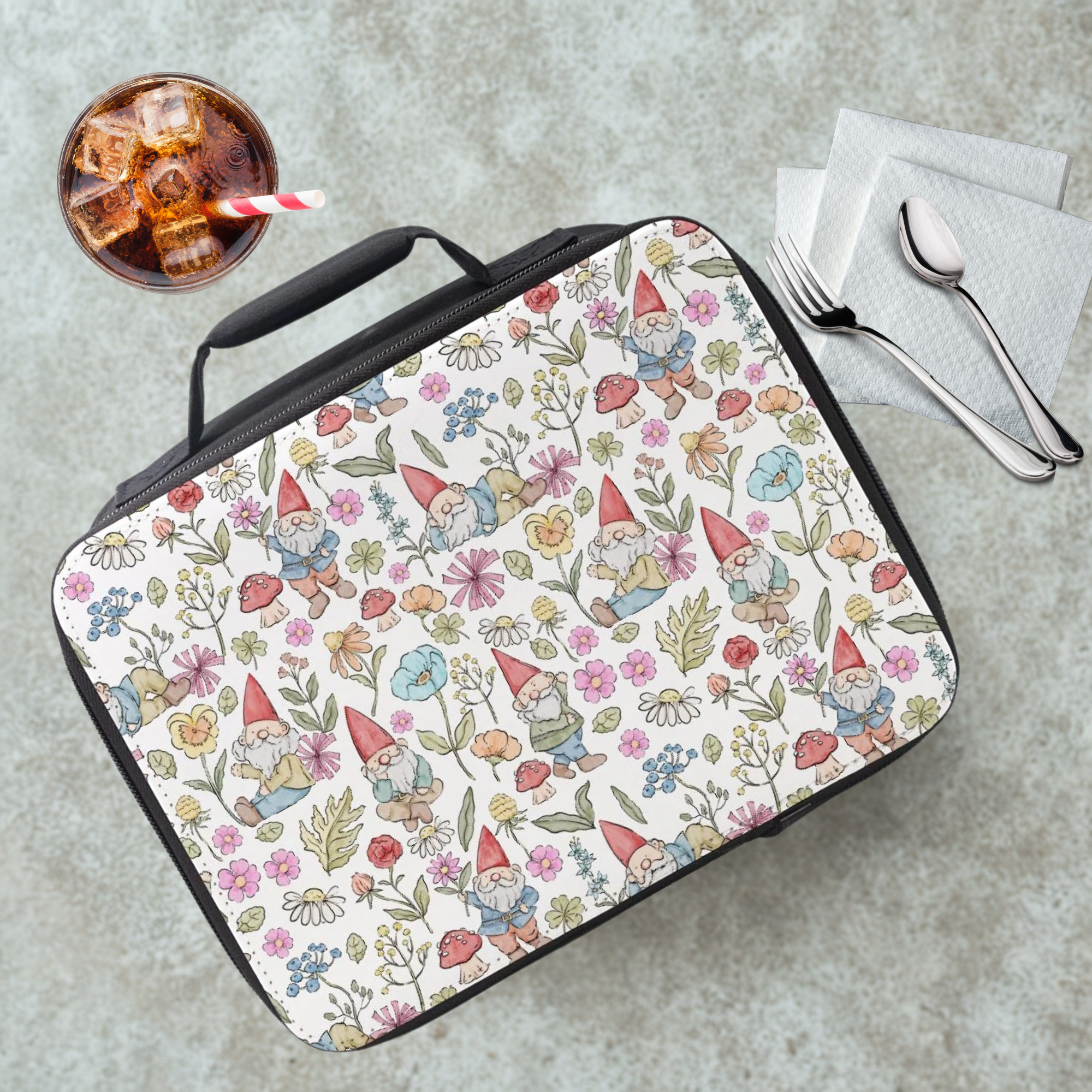 Insulated lunch bag with gnome and floral pattern on a cafeteria table with a drink and eating utensils.
