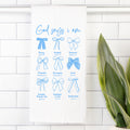 Tea Towel with blue bows and text on a white tiled wall with a plant.