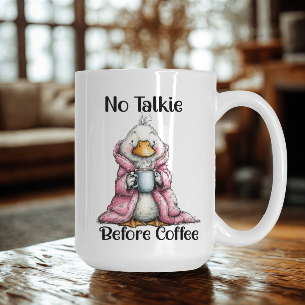White mug with a cartoon goose in a pink robe and text 'No Talkie Before Coffee' on a wooden table.