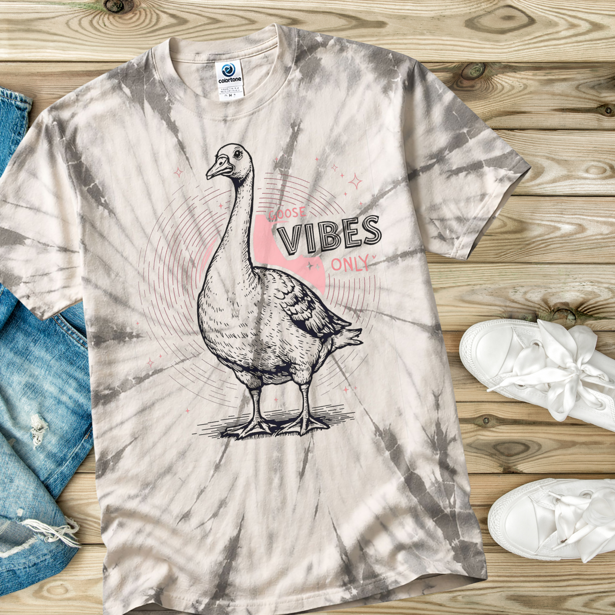 Spider Silver Tie-dye t-shirt with a goose graphic and text on a wooden surface with jeans and sneakers.