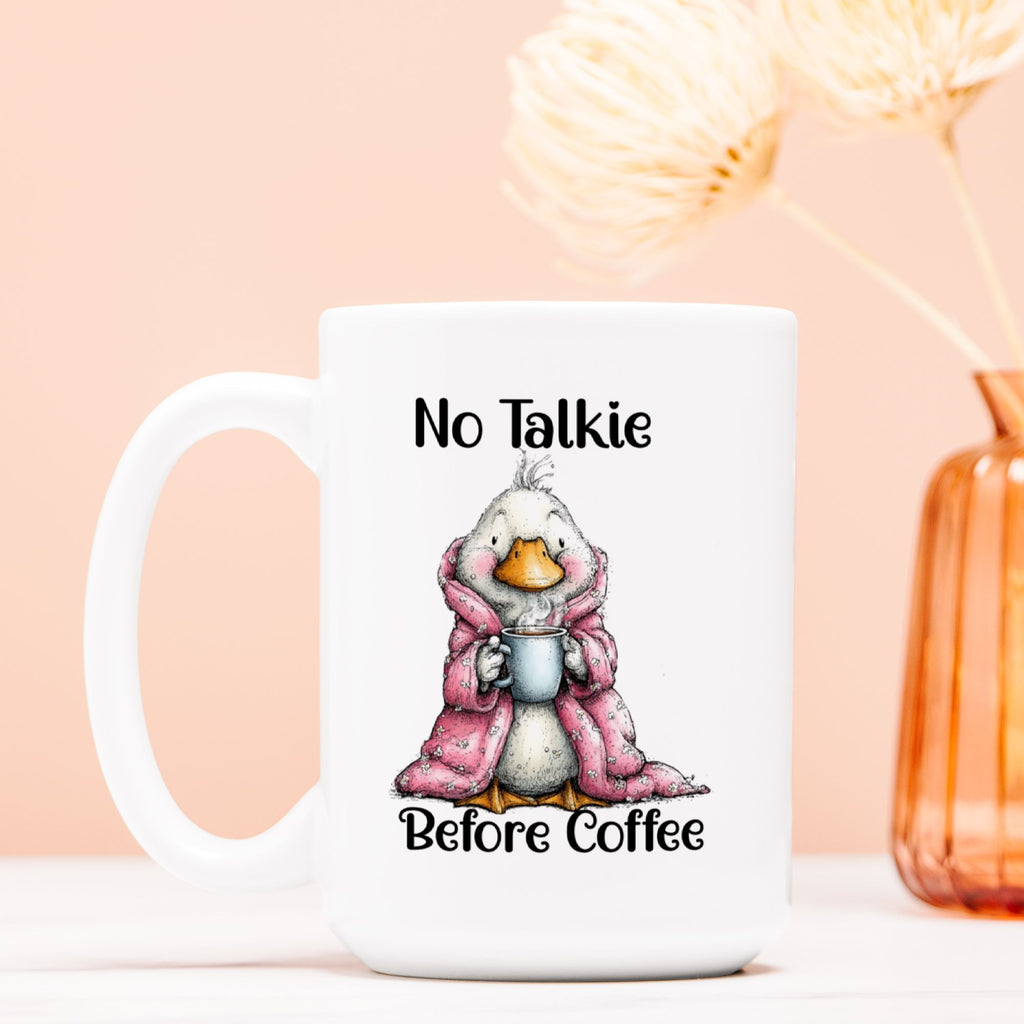 White mug with a cartoon duck in a pink robe holding a coffee cup, text 'No Talkie Before Coffee' on a peach background.