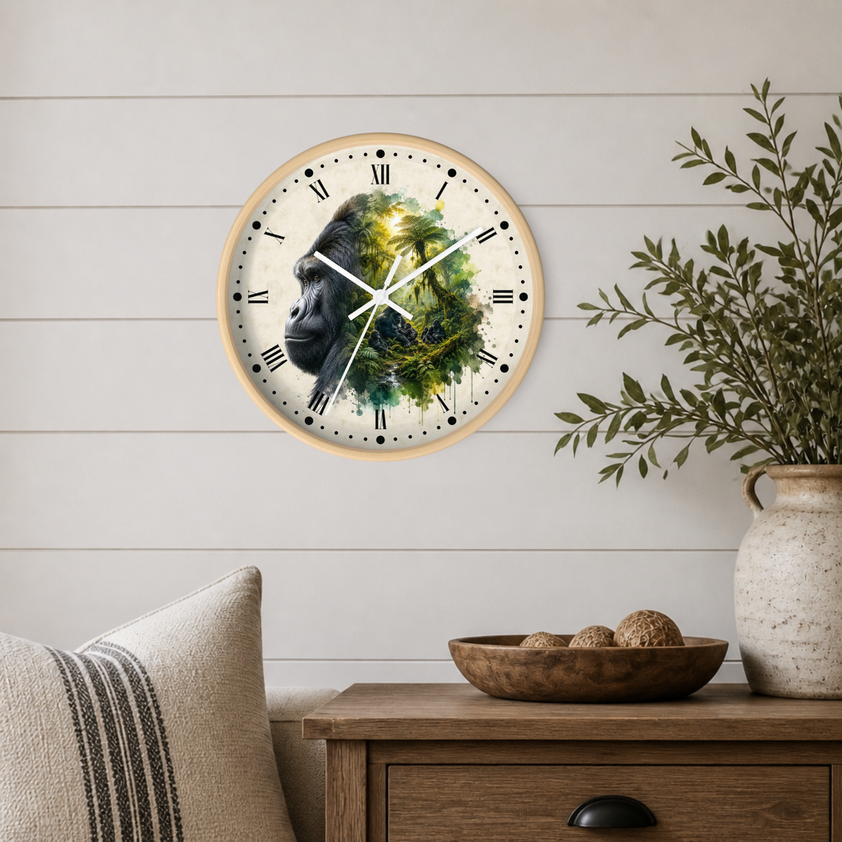A round wall clock with a light wood frame hangs on a white shiplap wall above a wooden side table. The clock face features a detailed illustration of a gorilla's face composed of green leaves and dark black tones, with black Roman numerals and white hands.