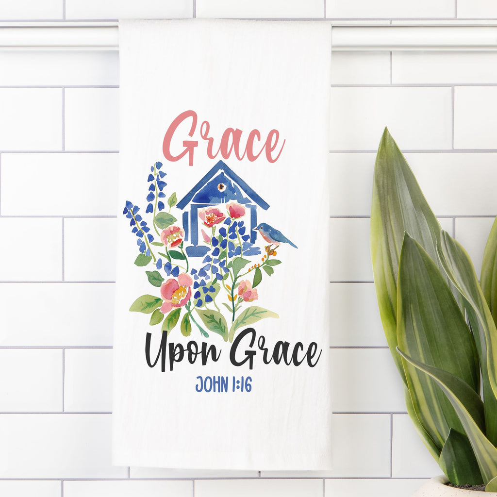 Decorative tea towel with floral design and 'Grace Upon Grace' text on a white tiled wall.