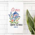 Decorative tea towel with floral design and 'Grace Upon Grace' text on a white tiled wall.