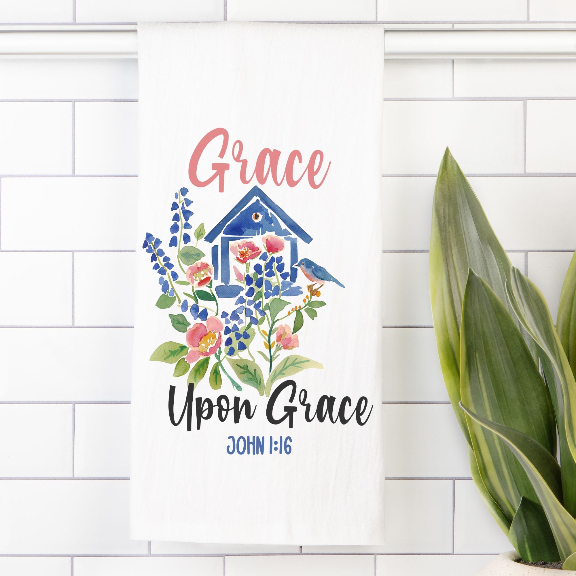 Decorative tea towel with floral design and 'Grace Upon Grace' text on a white tiled wall.