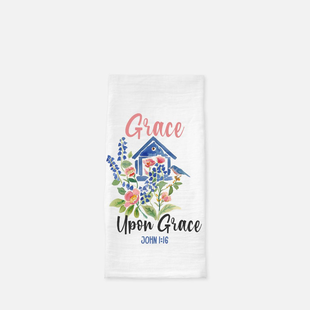 Decorative tea towel with a blue birdhouse, bird, and floral design, featuring the text 'Grace Upon Grace John 1:16' on a white background.