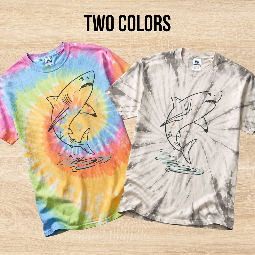 Two tie-dye t-shirts in the colors Eternity and Spider Silver with hand drawn shark designs on a wooden surface.