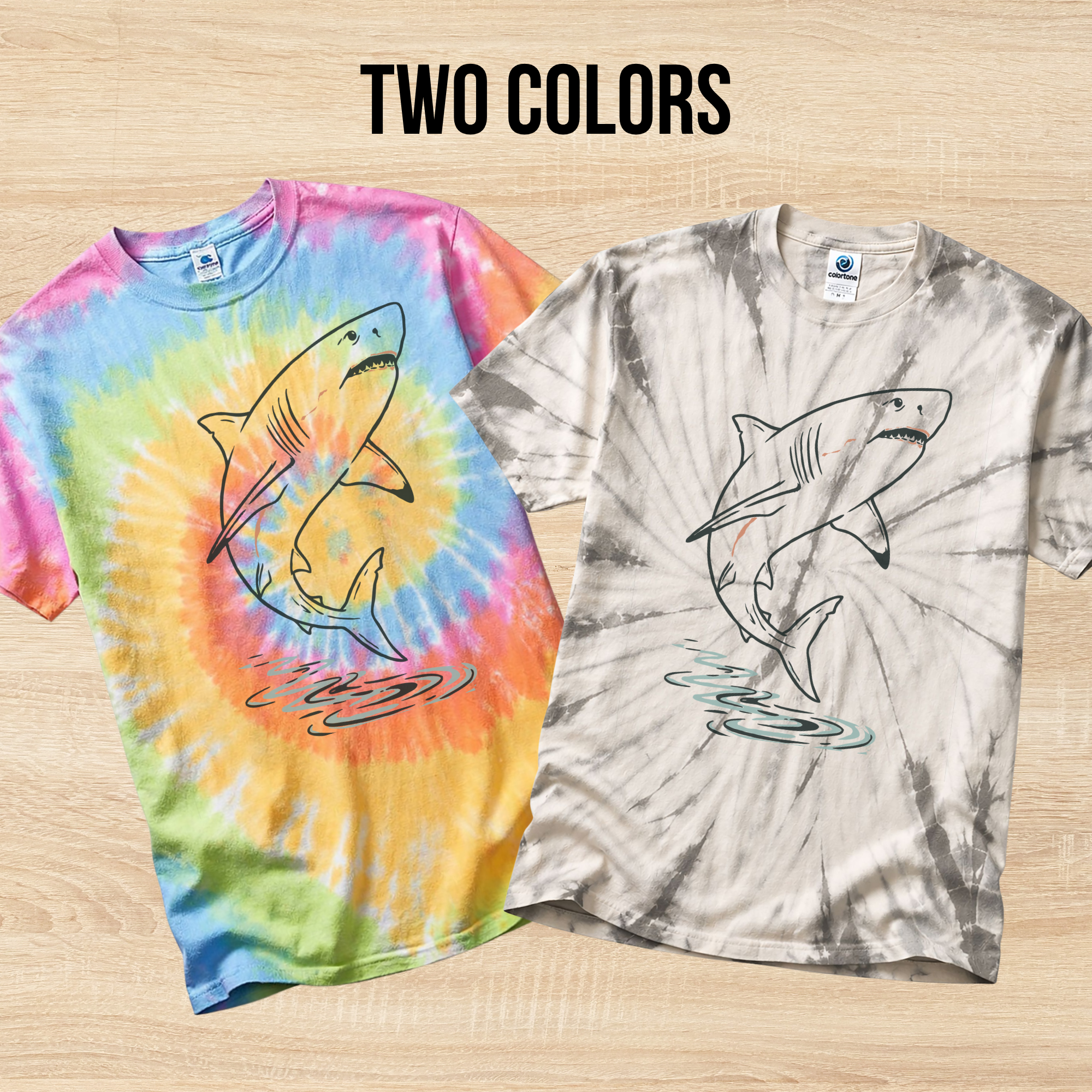 Two tie-dye t-shirts in the colors Eternity and Spider Silver with hand drawn shark designs on a wooden surface.