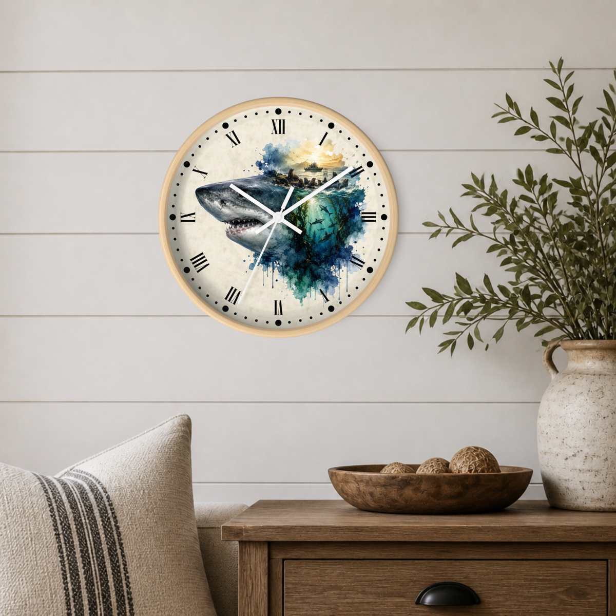 A round wall clock with a light wood frame hangs on a white shiplap wall above a wooden side table. The clock face features a watercolor design of a shark blending into blue and green water with a yellow sky.